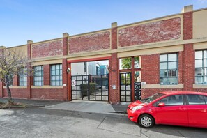 Une voiture rouge est garée devant un immeuble à la façade en briques et aux grandes fenêtres.