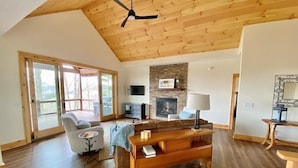 Un salón comedor amplio con techo de madera, chimenea, televisor y un ventanal grande.