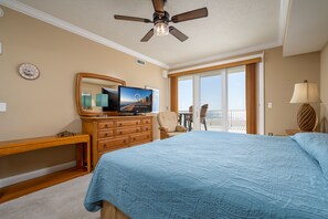 Una camera da letto con un letto grande, un ventilatore a soffitto, una televisione, un comò in legno, una sedia e vista sull'esterno.