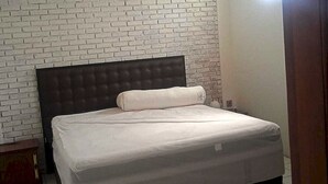 A bedroom with a brick-patterned wall, a dark headboard, and a white mattress. - EXPRESS O 92299 Bumi Bati Deudeuh (Bandung)