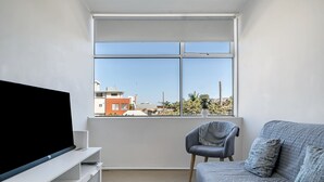 A modern living room with a large window, a flat-screen TV, a grey sofa, and a chair. - Quaint 1BD on the Doorstep of Manly Beach (Manly)