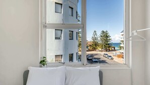 A bedroom with a large window, a bed with white bedding, and a view of a building and street outside. - Quaint 1BD on the Doorstep of Manly Beach (Manly)