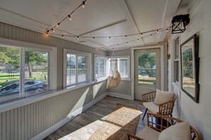 Une véranda avec de grandes fenêtres, un fauteuil suspendu et des guirlandes lumineuses.