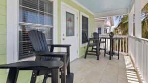 A covered porch with two Adirondack chairs, a small table, and a door with a decorative glass panel. - KeyLime Downtown Gulf View-FREE Golf Cart for 2026 (Cedar Key)