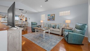 A modern living room with a flat-screen TV, a dining area with a chandelier, and a sofa set. - KeyLime Downtown Gulf View-FREE Golf Cart for 2026 (Cedar Key)