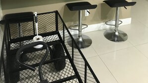 Ett modernt kök med ett kylskåp i rostfritt stål, en mikrovågsugn och en spis. Det finns tre hängande taklampor, en svart metallpall och ett svart metallställ med köksredskap.