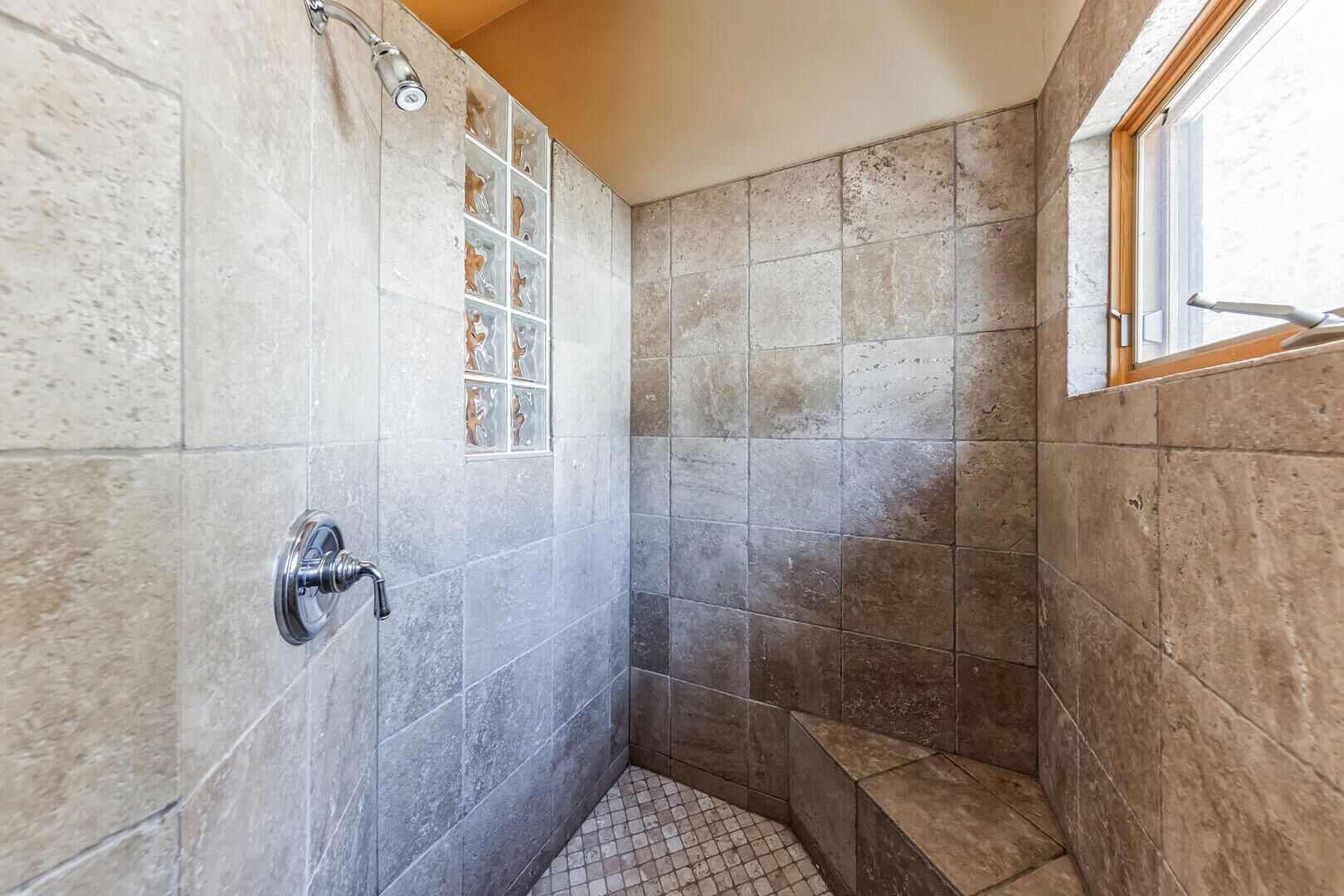 A shower with a glass door, tiled walls, and a window.