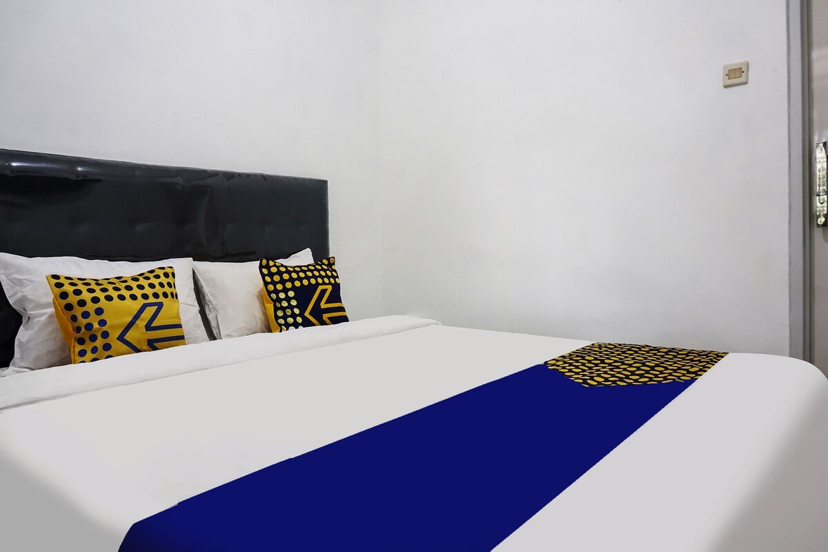 Una cama bien tendida con ropa de cama blanca y azul, dos almohadas con diseños geométricos y un cabecero oscuro.