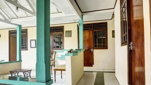 A covered outdoor area with a tiled floor, a wooden door, and a window with bars. - Hotel O Wisma Asri Putra Syariah (Ciampia)