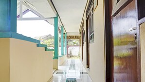 A corridor with tiled flooring, a wooden door, and a view of a mountainous landscape through an open area. - Hotel O Wisma Asri Putra Syariah (Ciampia)