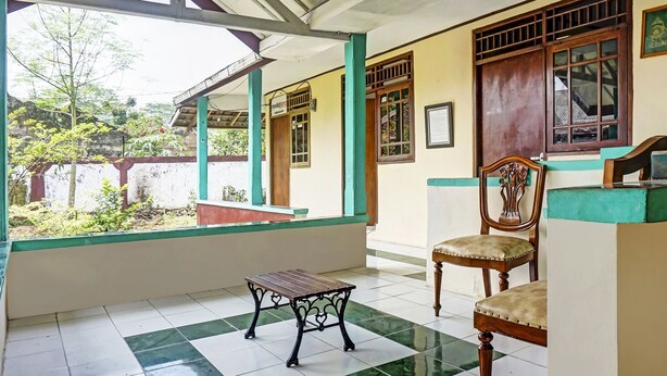 A room with a checkered floor, a wooden table, a wooden chair, and a window with a view of greenery outside. - Hotel O Wisma Asri Putra Syariah (Ciampia)