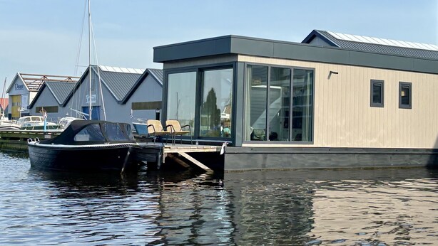 A modern floating house with a glass facade, docked near a marina with boats. - Harboursuite 2 incl. motorboot by Interhome (Woudsend)