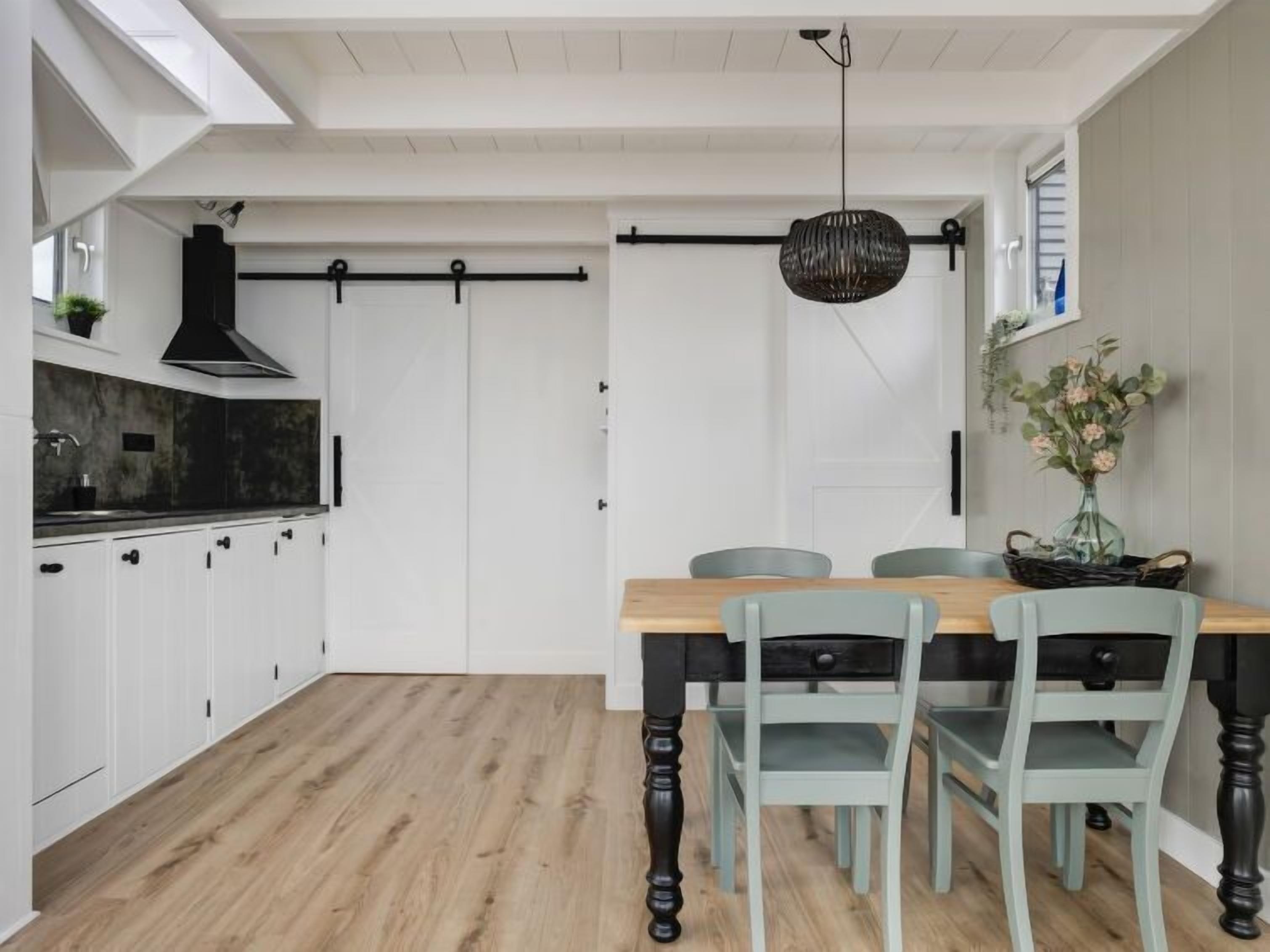 Una cocina moderna con armarios blancos, una mesa de comedor de madera y una lámpara colgante.