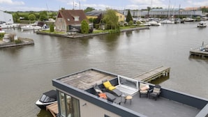 A modern floating house with a rooftop deck, a small boat docked at the front, and a marina in the background. - Harboursuite 2 incl. motorboot by Interhome (Woudsend)