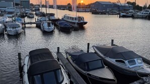 A marina with various boats docked, a building in the background, and a sunset. - Harboursuite Woudsend incl. motorboot by Interhome (Woudsend)