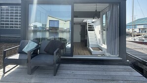 A modern, glass-enclosed structure with a wooden deck, a bench, and a staircase leading to an upper level. - Harboursuite Woudsend incl. motorboot by Interhome (Woudsend)