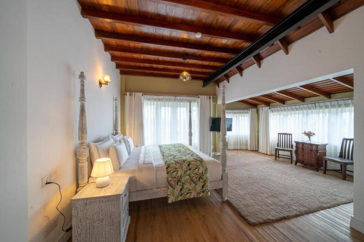 Ein Schlafzimmer mit Holzbalkendecke, einem Bett mit Blumenmuster-Überwurf, einem Nachttisch mit Lampe und Blick auf den angrenzenden Essbereich.