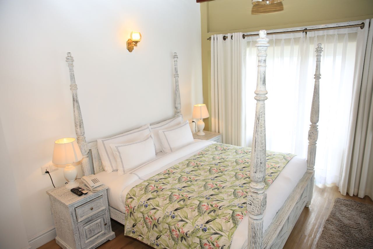 Een hemelbed met een bloemenbedekker, nachtlampjes en een nachtkastje met een telefoon.