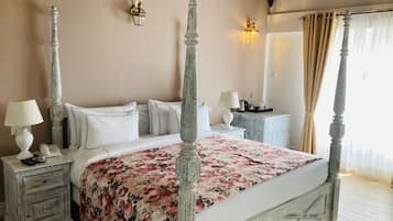 A four-poster bed with a floral bedspread, bedside tables with lamps, and a nightstand with a telephone.