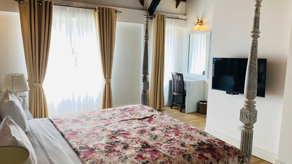 A bedroom with a four-poster bed, a television on the wall, and a desk with a chair.