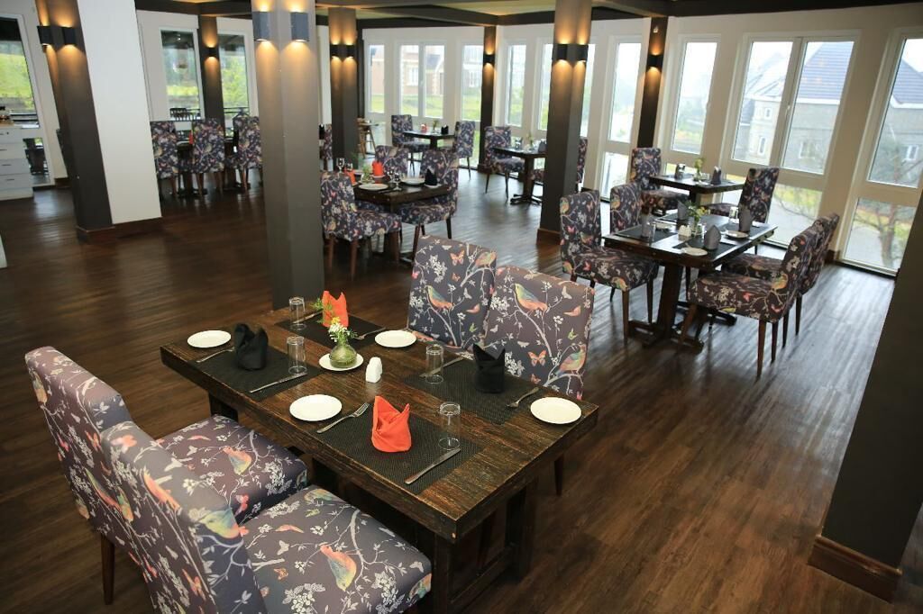 A dining area with multiple tables and chairs, large windows, and a wooden floor.