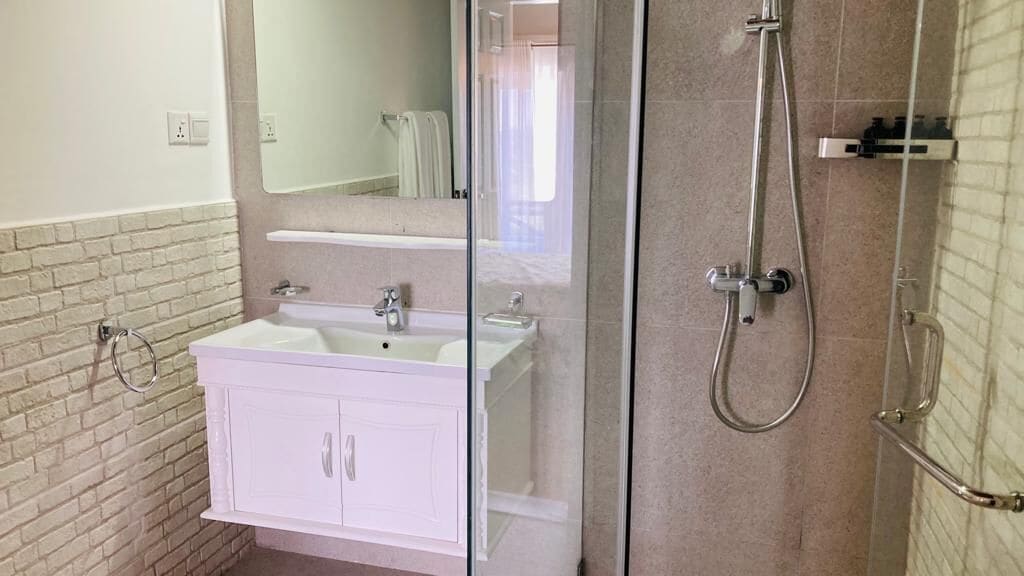 Une salle de bain avec un meuble-lavabo blanc, une cabine de douche en verre et une zone de douche carrelée.