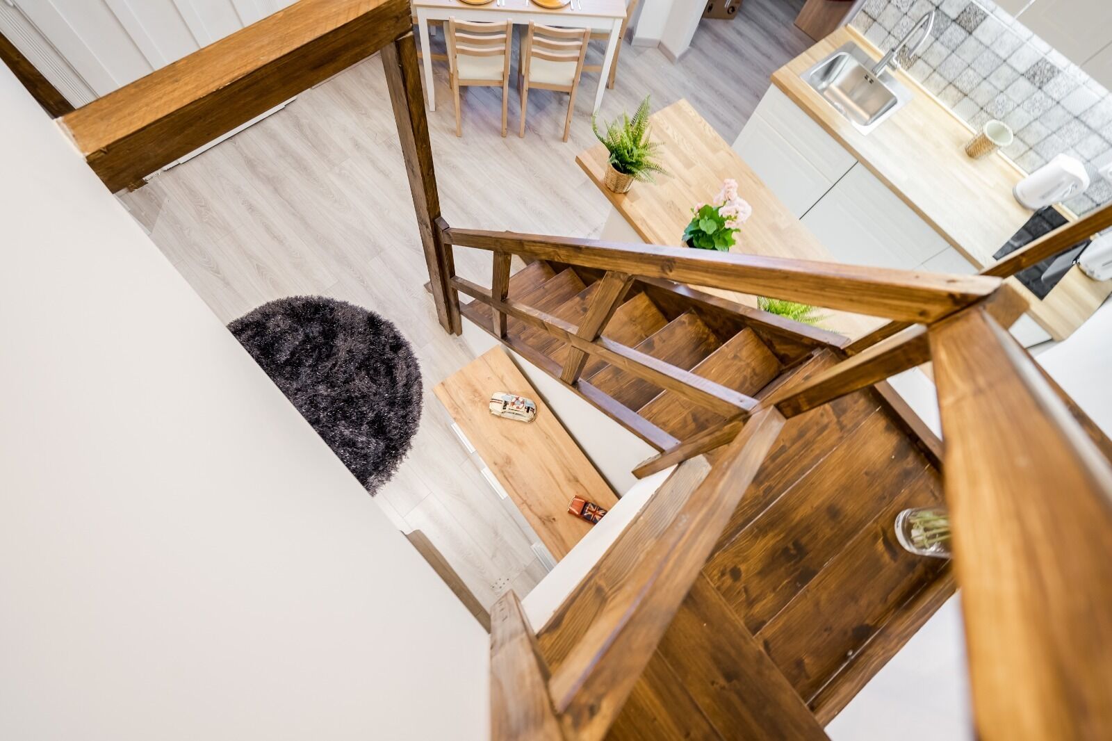 A modern kitchen with wooden flooring, a dining area with chairs, and a staircase with wooden railings.
