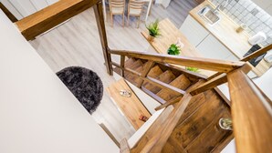 Una cocina moderna con suelo de madera, un comedor con sillas y una escalera con barandilla de madera.