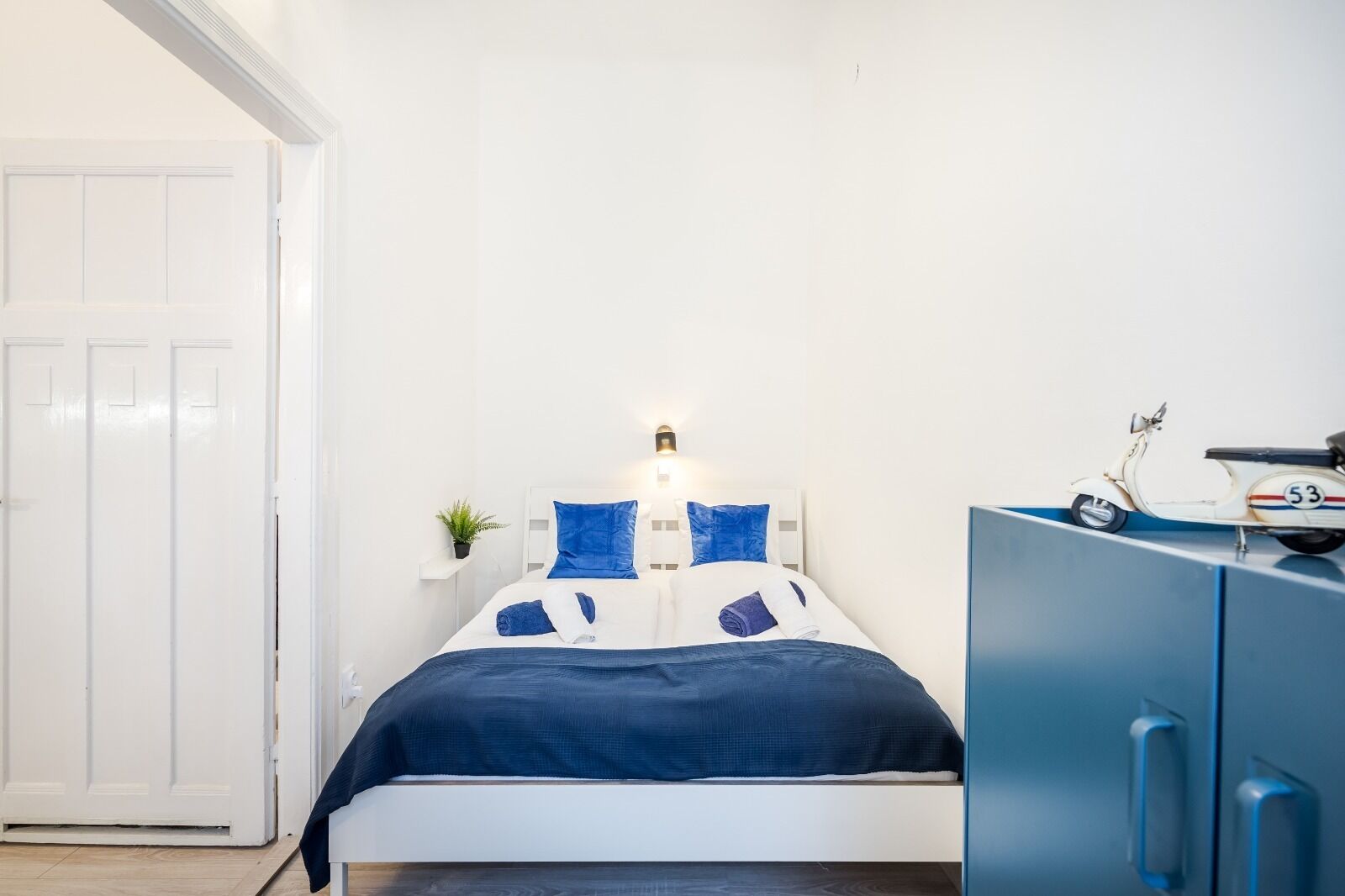 Un dormitorio con cama, mesita de noche, lámpara, planta en maceta y una patineta.