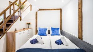 Un dormitorio con escalera de madera, una cama con ropa de cama azul y blanca, y una mesita de noche con un jarrón de flores.