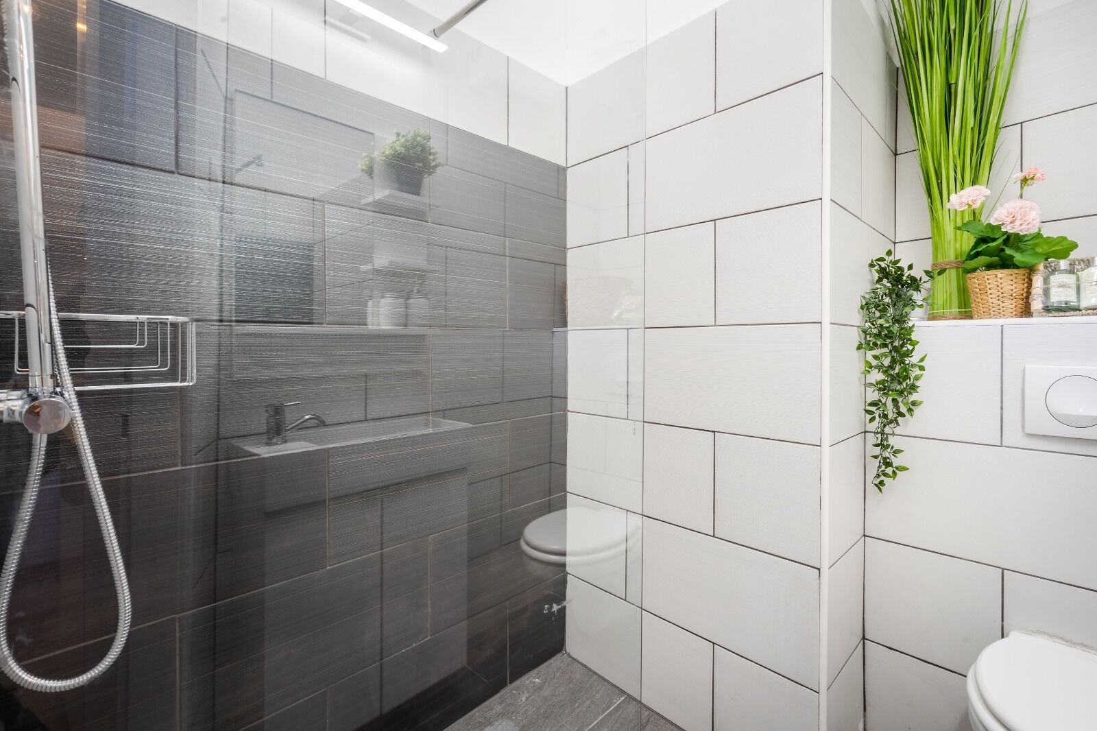 A modern bathroom with a glass-enclosed shower, white tiled walls, and a toilet.