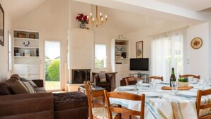 A spacious living room with a fireplace, a dining area with a table set for four, and a television on a stand. - Les Agapanthes by Interhome (Dinard)