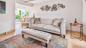 A spacious living room with a grey sofa, a matching ottoman, and a colorful rug. There is a dining area visible through an open door, and a wall decorated with circular mirrors. - Blue Crab by Interhome (Mevagissey)