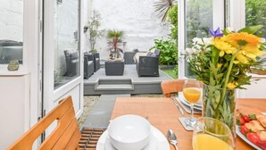 A sunlit patio with outdoor seating, a dining table set for two, and a variety of plants and flowers. - Blue Crab by Interhome (Mevagissey)