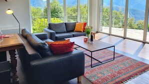 Un salon moderne avec un canapé, une table basse et une vue sur les montagnes, visible à travers de grandes fenêtres.