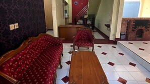 A spacious living room with a red sofa set, a wooden coffee table, and a patterned carpet. A staircase leads to an upper floor, and a fireplace is visible in the background. - Hotel O Pahlawan Udyana Syariah (Sentul City)