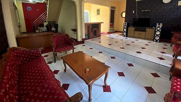 A spacious living room with a red sofa, a wooden coffee table, and a tiled floor. There is a staircase leading to another room, a fireplace, and a television set. - Hotel O Pahlawan Udyana Syariah (Sentul City)
