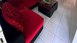 A living room with a red sofa, a coffee table, and a television on a stand. - Hotel O Pahlawan Udyana Syariah (Sentul City)