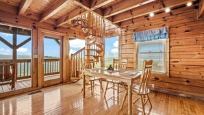 L’intérieur d’un chalet en bois comprend une table à manger, des chaises, un escalier en colimaçon et de grandes fenêtres offrant une vue panoramique.