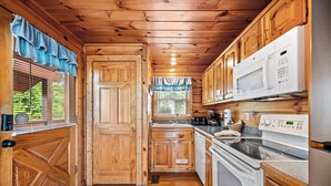 Une cuisine de style rustique, avec des éléments en bois, comprenant un four à micro-ondes, une cuisinière et un évier intégrés.