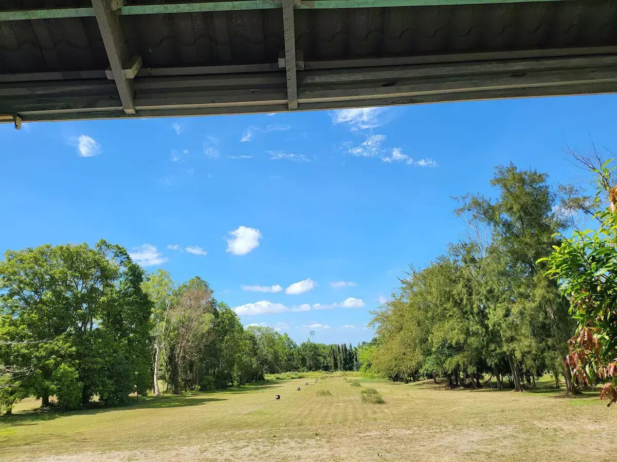 A covered outdoor area with a view of a grassy field and trees under a clear sky.