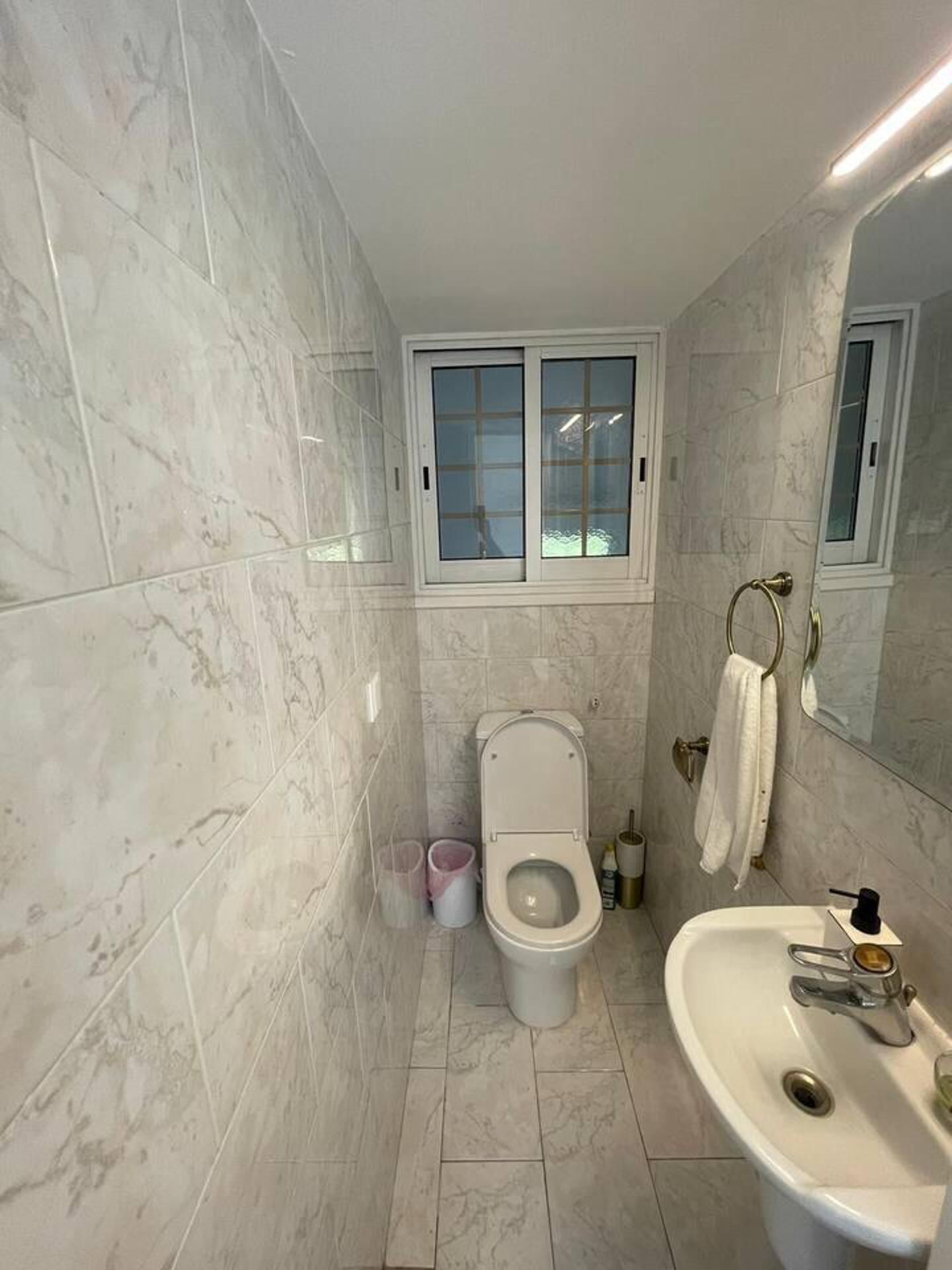 Un baño con inodoro, lavamanos y una ventana sobre el inodoro.
