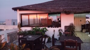 A building with a thatched roof, large windows, and outdoor seating. - Residence Hotel Kakatar (Dakar)