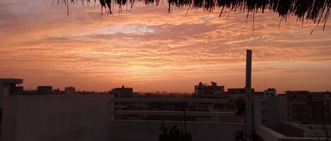 A rooftop terrace with a view of a sunset over a cityscape.