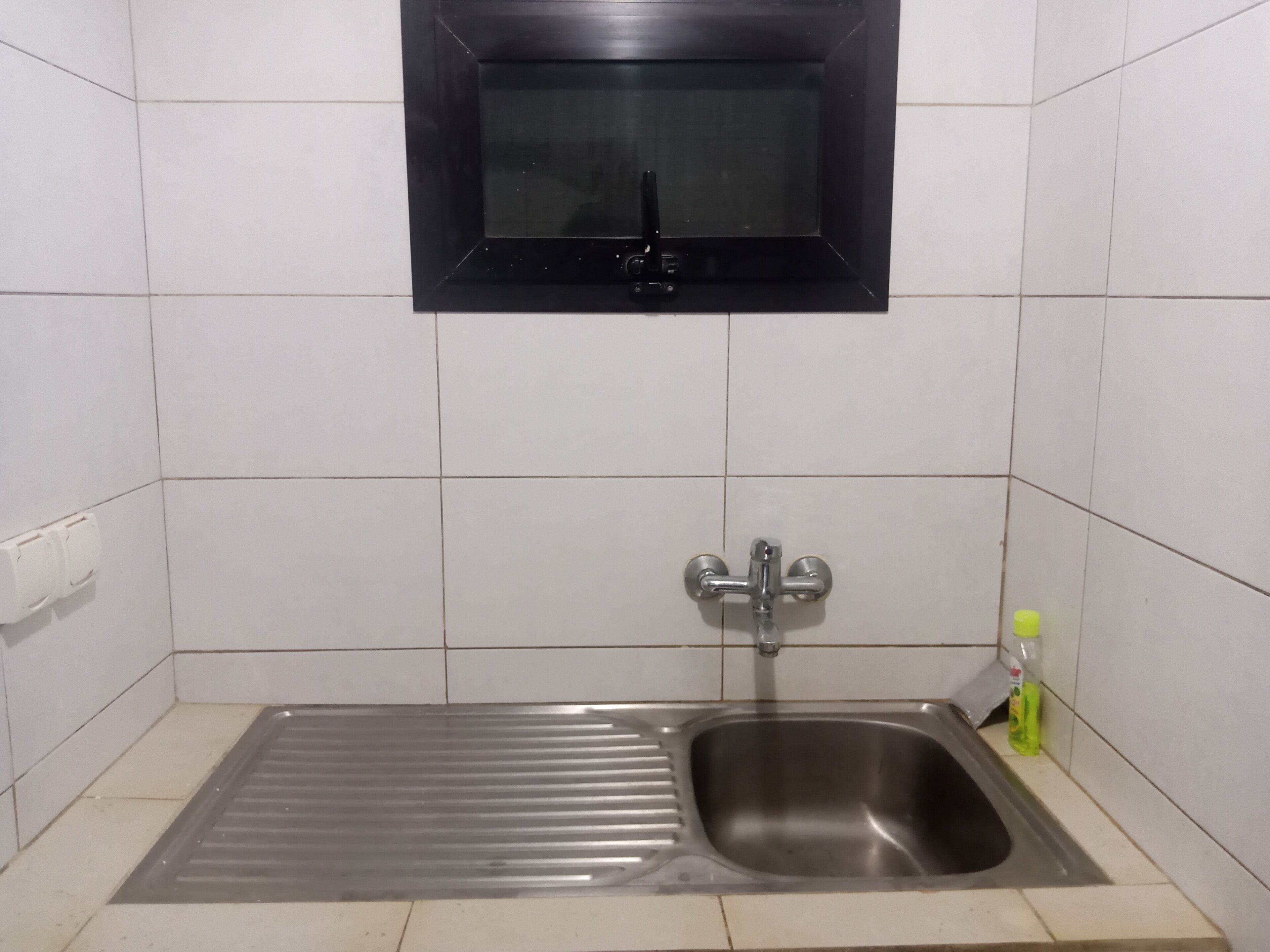 A kitchen with a stainless steel sink, a black window above it, and a white tiled backsplash.