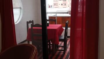 Un comedor con una mesa preparada para dos personas, una ventana y vistas a edificios.