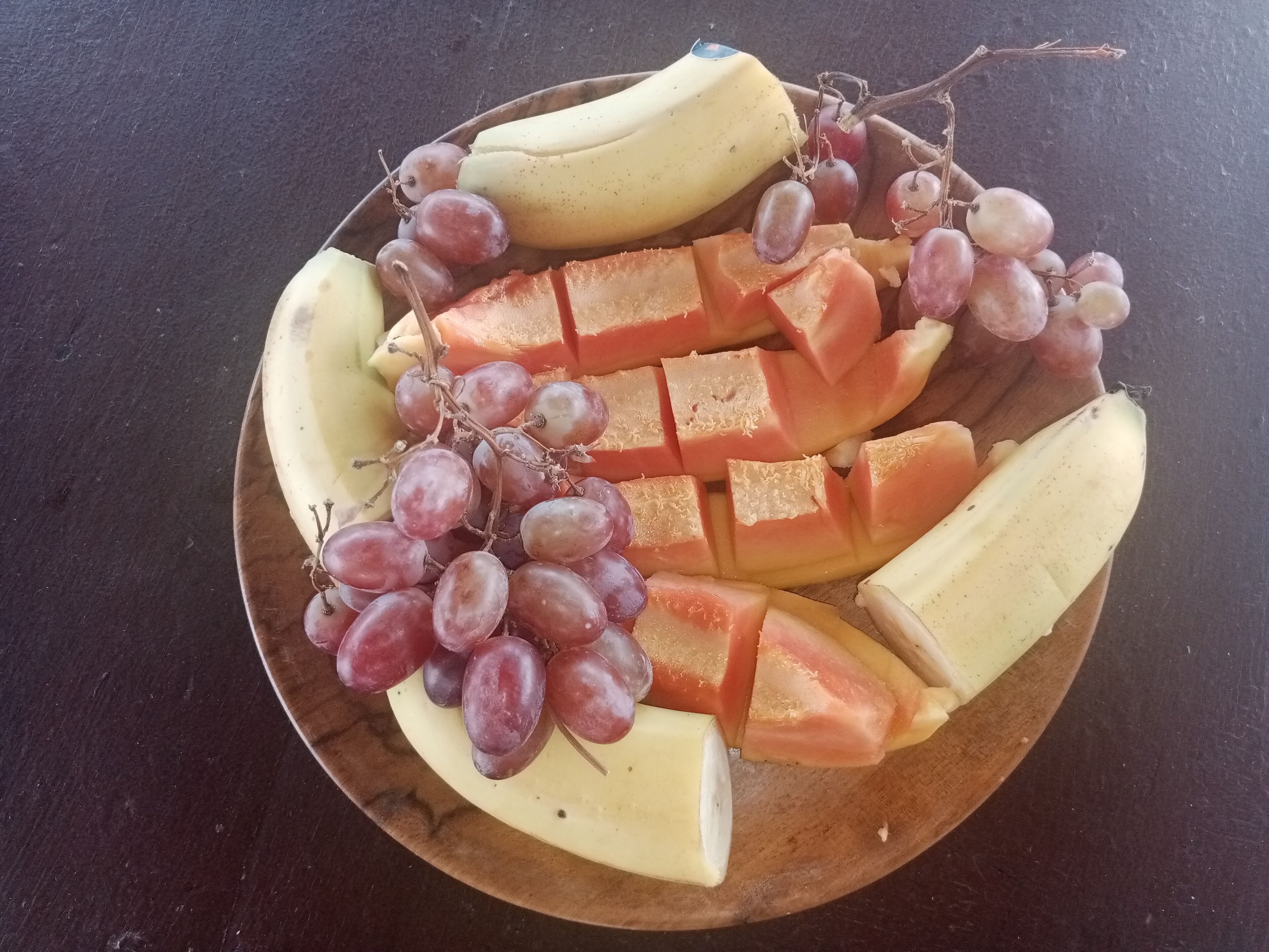 Un plato de madera con frutas en rodajas y uvas.