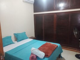 Un dormitorio con cama, dos almohadas, una manta y un ventilador.