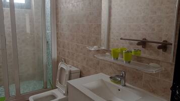 A bathroom with a toilet, sink, and shower. There are green cups on a shelf above the sink.