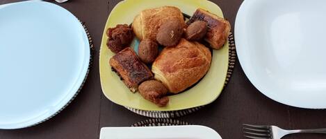 A table with plates of food, including fruits, pastries, and a white plate with cubed fruit.